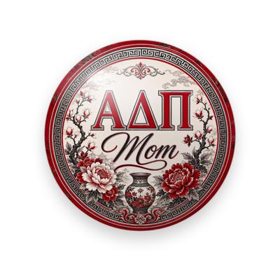 Alpha Delta Pi #057 button. Cream center with a red Greek key border, red serif Greek letters, black script “Mom”, peonies, blossom branches and a vase.