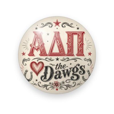 Alpha Delta Pi #080 button. Cream background with red western serif Greek letters, a red heart, black script “the Dawgs”, horseshoes, stars and scrollwork.