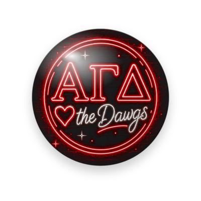 Alpha Gamma Delta #026 button. Black background inside a glowing red neon ring with red neon Greek letters, a neon heart, script “the Dawgs” and sparkles.