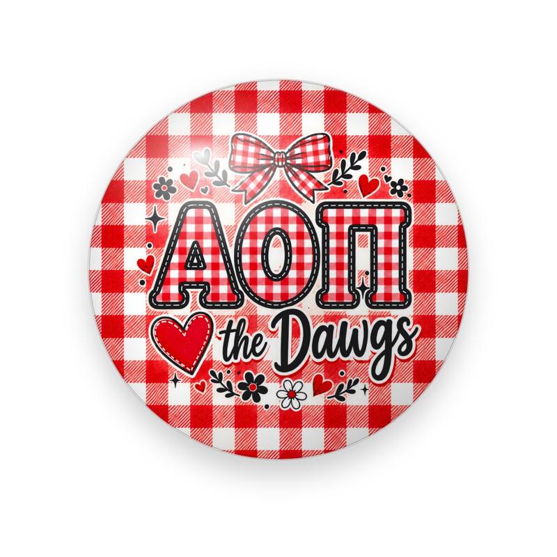 Alpha Omicron Pi #055 button. Red gingham background with a gingham bow, red gingham Greek letters outlined in black, a red heart, black script “the Dawgs” and flowers.