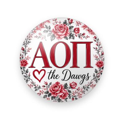 Alpha Omicron Pi #058 button. White background with a wreath of red roses and gray leaves around red serif Greek letters, a red heart outline and black script “the Dawgs.”