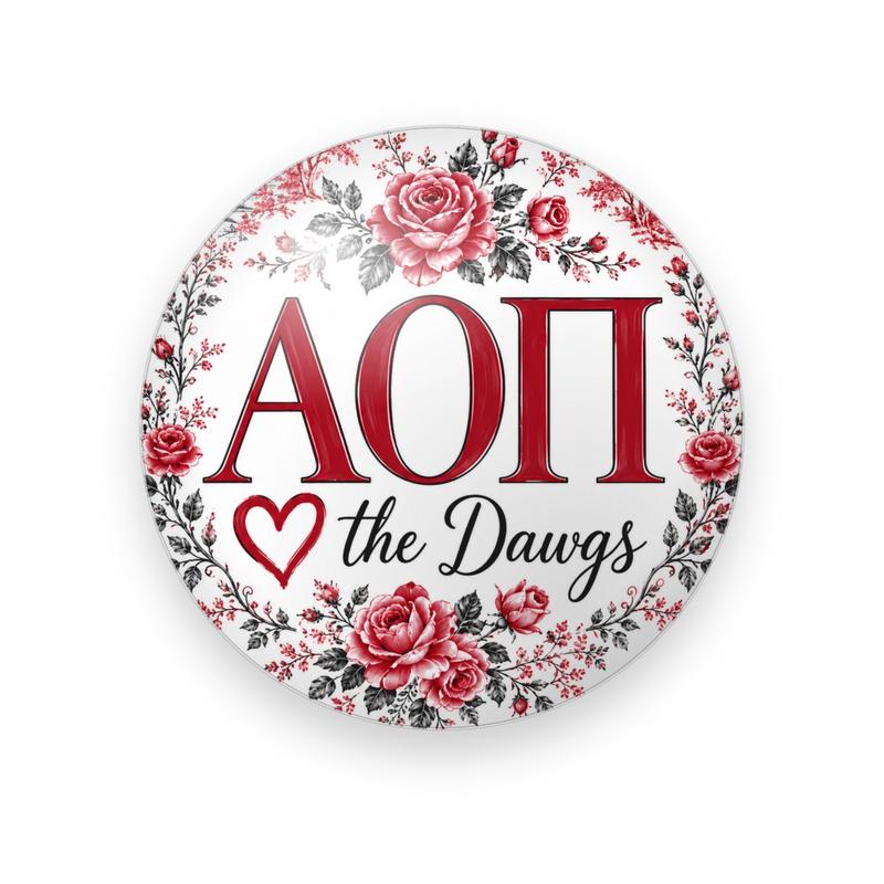 Alpha Omicron Pi #058 button. White background with a wreath of red roses and gray leaves around red serif Greek letters, a red heart outline and black script “the Dawgs.”