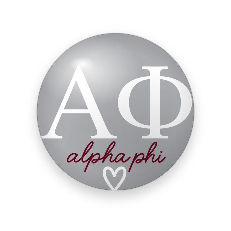 Alpha Phi #054 button. Silver gray background with large white serif Greek letters over the full name in lowercase maroon script and a small white outline heart.