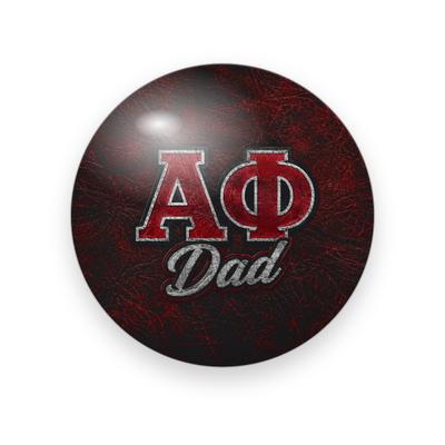 Alpha Phi #065 button. Dark red and black crackled leather background with red Greek letters outlined in silver above silver script “Dad.”