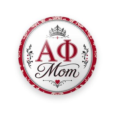 Alpha Phi #071 button. White background with a red damask border, red serif Greek letters, black script “Mom”, a black crown, flourishes, and a small red heart.