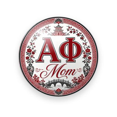 Alpha Phi #075 button. White background with a red Greek key border, red serif Greek letters, red script “Mom”, a pagoda, an arched bridge, vases, and red blossoms.