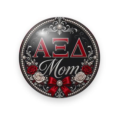 Alpha Xi Delta #041 button. Black background with red Greek letters, silver script “Mom”, red and ivory roses, a red satin bow, pearls, and silver filigree.