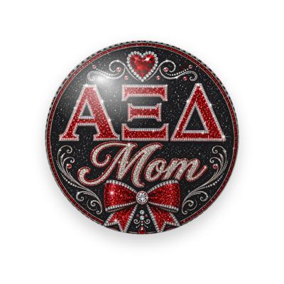 Alpha Xi Delta #043 button. Black glitter background with red rhinestone Greek letters, red script “Mom”, a red jeweled bow, a heart gem, and silver swirls.