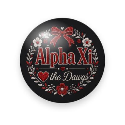 Alpha Xi Delta #049 button. Black background with red embroidered “Alpha Xi” lettering, a red bow, a heart, white script “the Dawgs”, and a wreath of red and white flowers.
