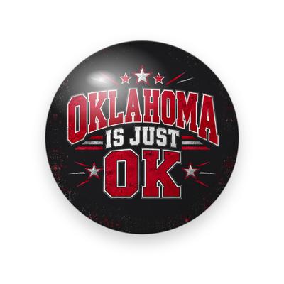 UGA #074 button. Black background with red stars and rays behind “Oklahoma Is Just OK” in red arched varsity and white block capitals.