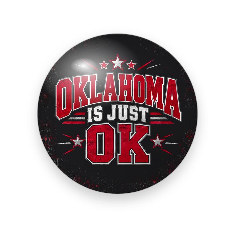 UGA #074 button. Black background with red stars and rays behind “Oklahoma Is Just OK” in red arched varsity and white block capitals.